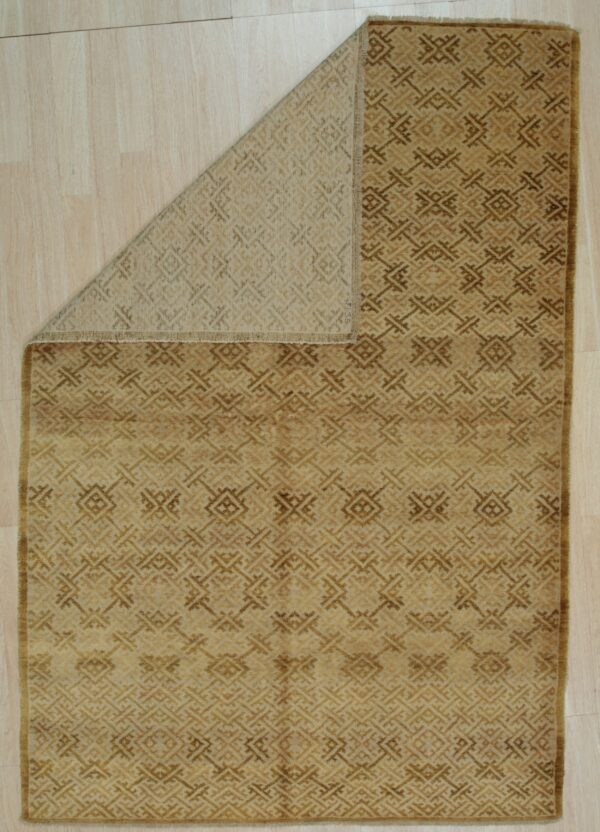 Golden brown rug with a repeating geometric pattern is folded back, revealing the tan backing on light wood flooring.