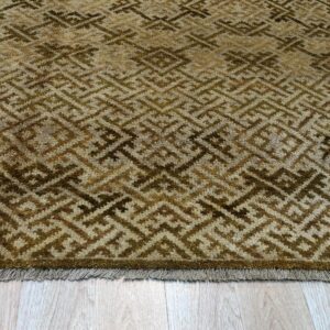 Textured brown and beige rug with a repeating diamond key pattern on light wood flooring.