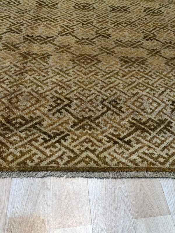 Textured brown and beige rug with a repeating diamond key pattern on light wood flooring.