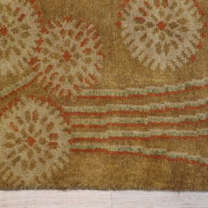 Close-up of a golden brown rug with abstract floral and striped patterns on light wood flooring.