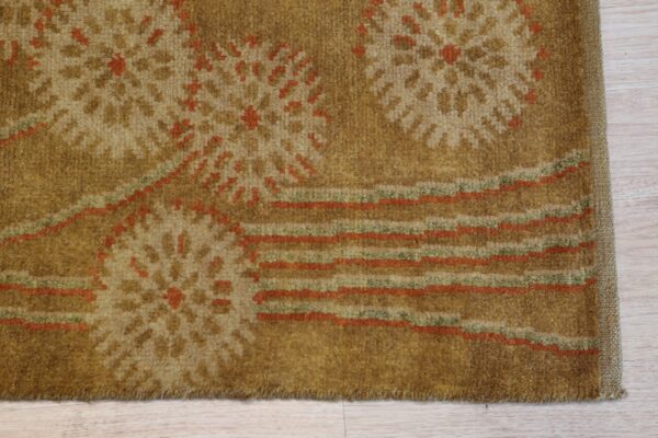 Close-up of a golden brown rug with abstract floral and striped patterns on light wood flooring.