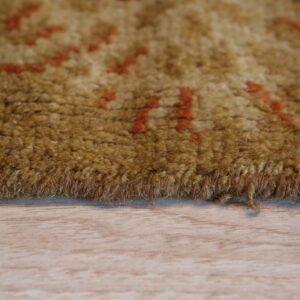 Close-up of a thick, golden-brown rug with blurry orange patterns resting on a light wood floor.