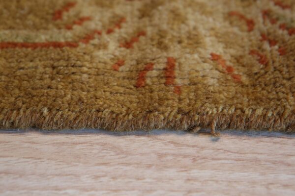 Close-up of a thick, golden-brown rug with blurry orange patterns resting on a light wood floor.