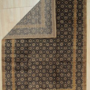 A dark brown geometric rug with tan accents is folded back on light wood plank flooring.