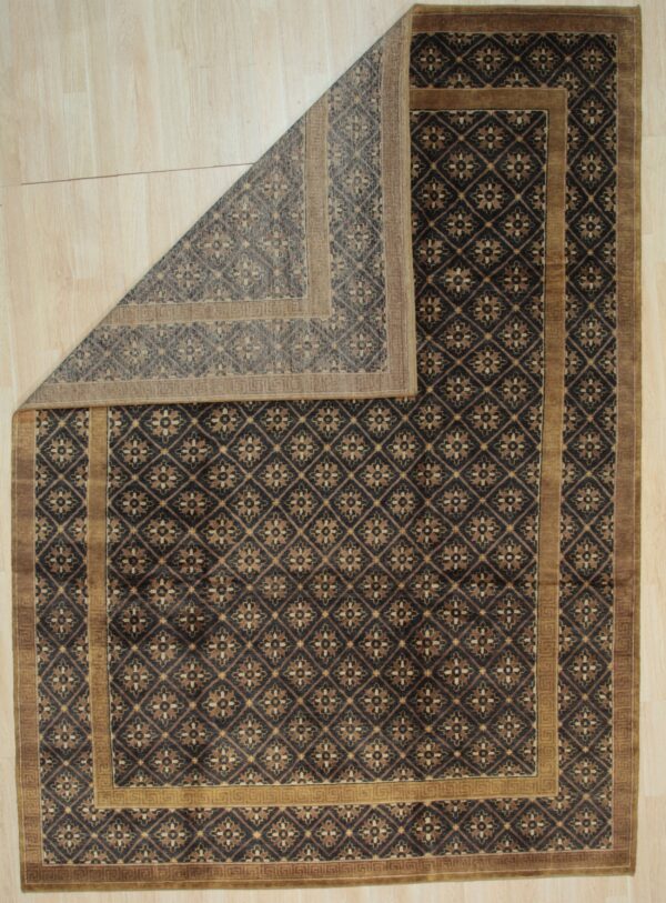 A dark brown geometric rug with tan accents is folded back on light wood plank flooring.