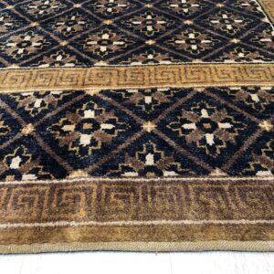 Black, brown, and cream diamond patterned rug with a golden Greek key border on light flooring.