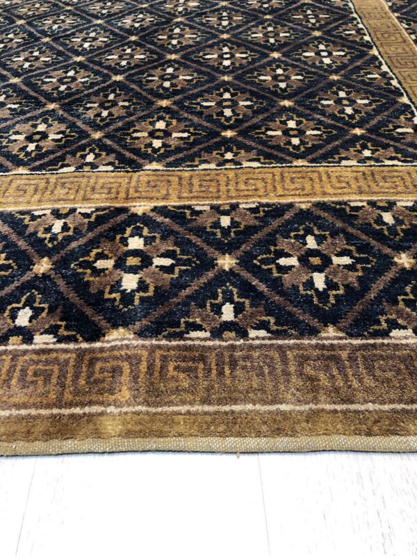 Black, brown, and cream diamond patterned rug with a golden greek key border on light flooring.