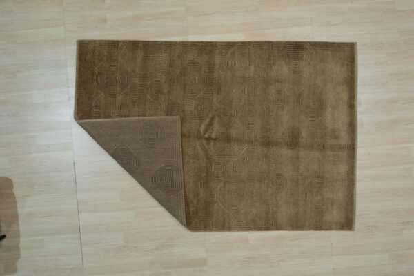 Brown geometric rug on light wood flooring, featuring concentric patterns with one corner turned back.