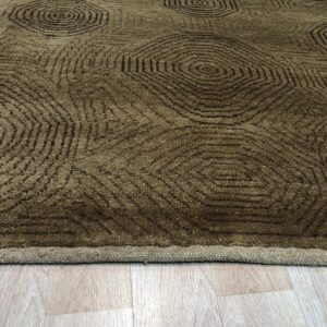 A textured olive rug with repeating dark geometric circles rests on pale blonde plank flooring.