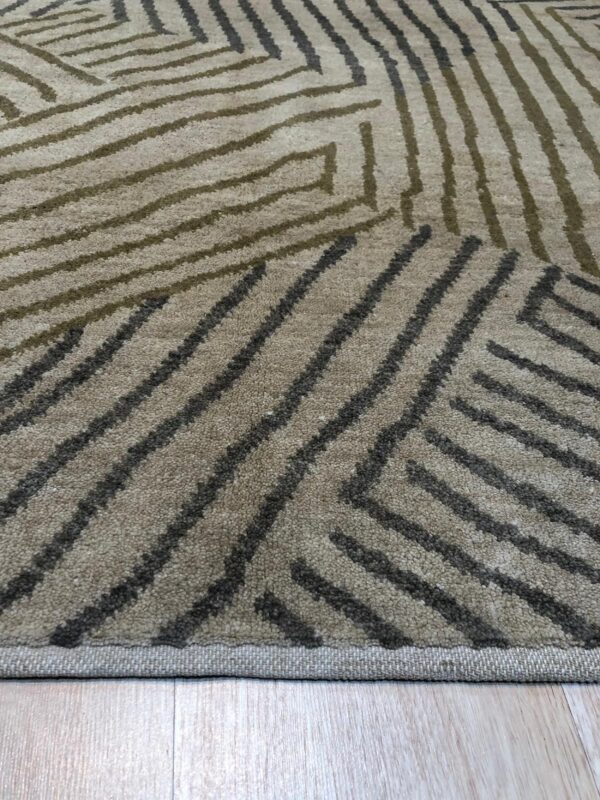 Close-up of a tan rug with an abstract linear pattern in olive green and dark gray over light wood flooring.