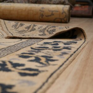 Cream and blue patterned rug partially unrolled on a wood floor, showing the low pile and woven backing.