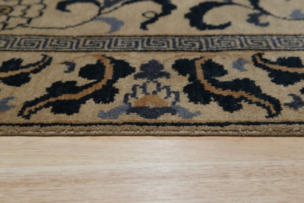Detail of a tan rug border featuring black, brown, and blue floral patterns on light wood flooring.