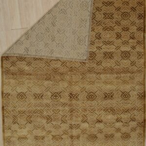 A tan and brown geometric rug lies on wood flooring with its woven backing visible from a folded corner.