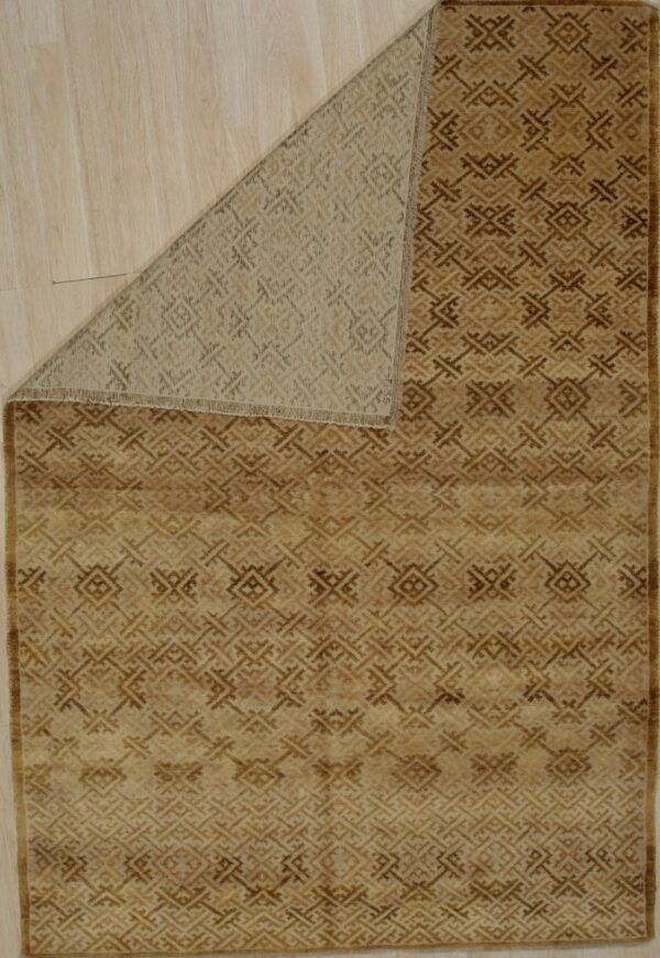 A tan and brown geometric rug lies on wood flooring with its woven backing visible from a folded corner.