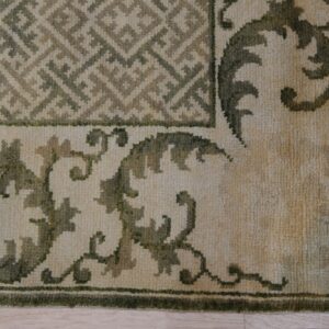 Textured rug corner featuring geometric and scrolling motifs in beige and varying shades of olive green.