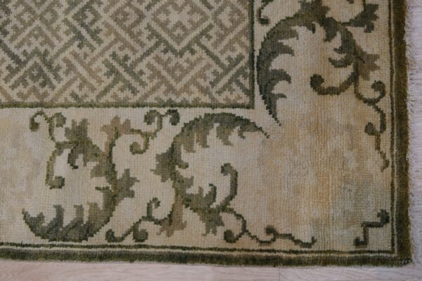 Textured rug corner featuring geometric and scrolling motifs in beige and varying shades of olive green.