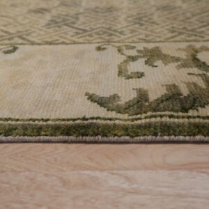 Close-up shows the low pile border of a cream and green patterned rug on light wood flooring.