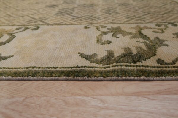 Close-up shows the low pile border of a cream and green patterned rug on light wood flooring.