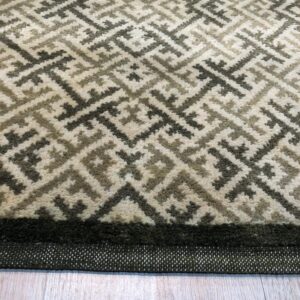 A medium pile rug with a geometric pattern in cream, gray, and tan rests on light wood planks.