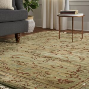 Muted green area rug with rust-colored traditional scrolling lies beneath a dark gray sofa and side table.