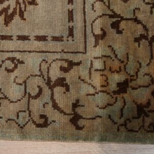 Medium pile rug border featuring tan, brown, and muted teal traditional patterns on wood floor.