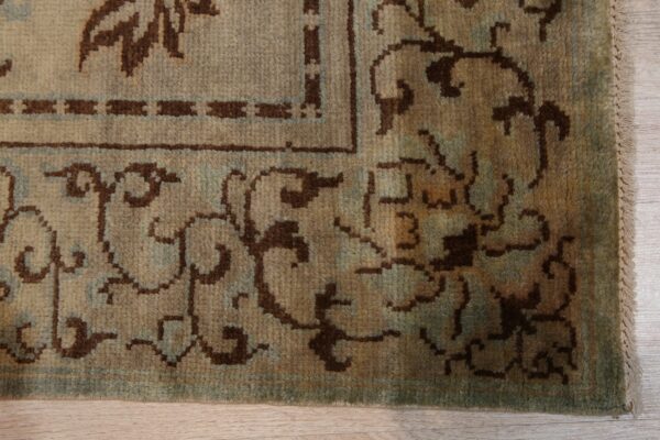 Medium pile rug border featuring tan, brown, and muted teal traditional patterns on wood floor.
