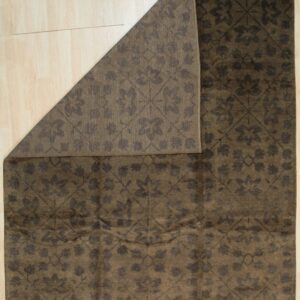 Dark brown rug with a tonal floral damask pattern displayed partially folded back on light wood flooring.