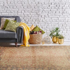 Orange and cream patterned rug under a gray sofa arm, set against a bright white brick wall.