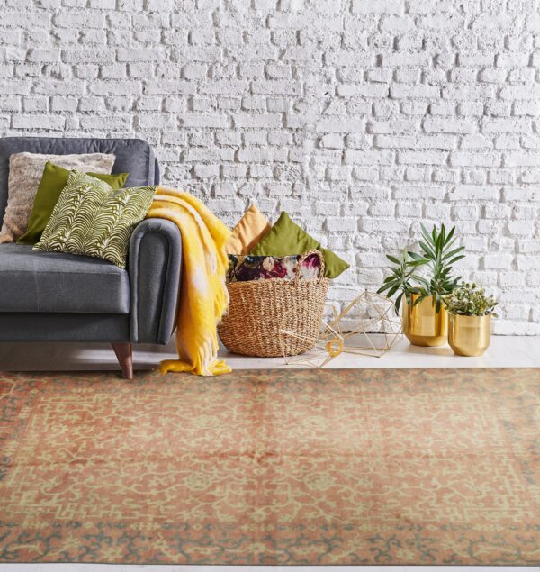 Orange and cream patterned rug under a gray sofa arm, set against a bright white brick wall.