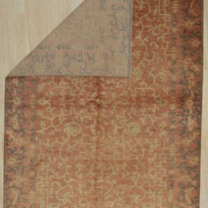 Orange and gold patterned rug displayed on light wood floor with a corner folded over.