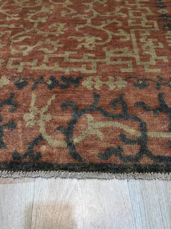 Close-up of a medium-pile rug featuring terracotta, sage, and dark gray patterns on light wood flooring.
