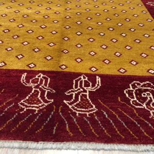 Gold rug with small geometric motifs and a maroon border showing stylized figures on a wood floor.