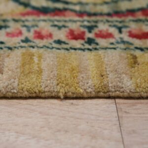 A medium-pile rug with beige, yellow, pink, and teal patterns is shown close-up on a wood floor.