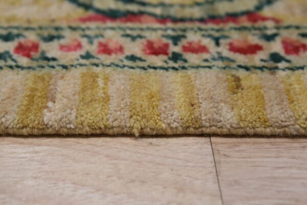 A medium-pile rug with beige, yellow, pink, and teal patterns is shown close-up on a wood floor.