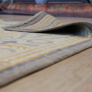 Low-pile cream rug with abstract gray and yellow patterning rests on light wood flooring.