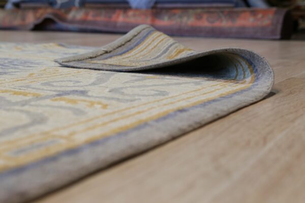 Low-pile cream rug with abstract gray and yellow patterning rests on light wood flooring.