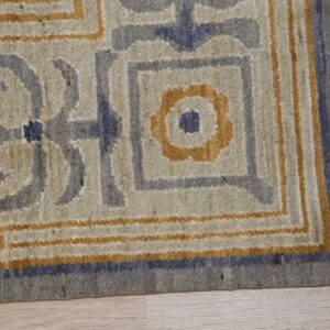 Textured rug corner displaying a geometric pattern in cream, gray, and ochre on light wood flooring.