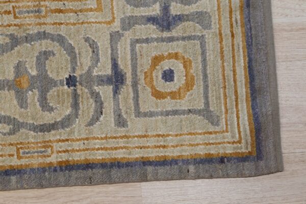 Textured rug corner displaying a geometric pattern in cream, gray, and ochre on light wood flooring.