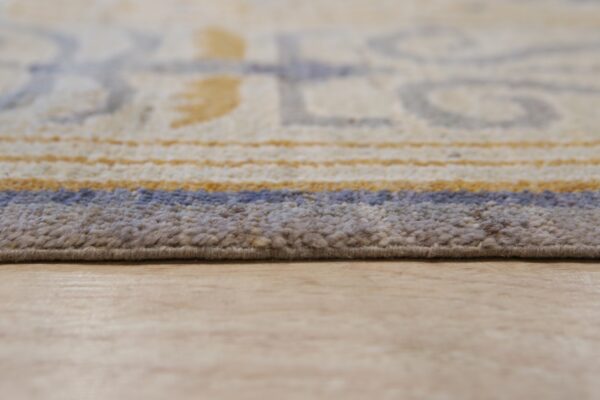 Textured tan and blue rug edge with blurred geometric patterns rests on a light wood plank floor.