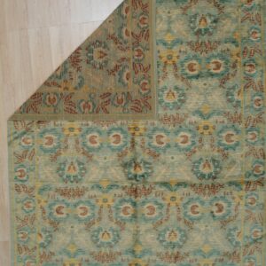 Medium pile teal rug with rust and gold traditional patterns, corner folded back on wood floor.