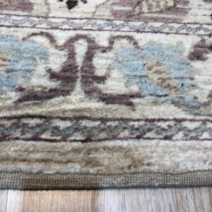 High-pile rug with cream, mauve, and blue traditional patterns rests on light plank flooring.