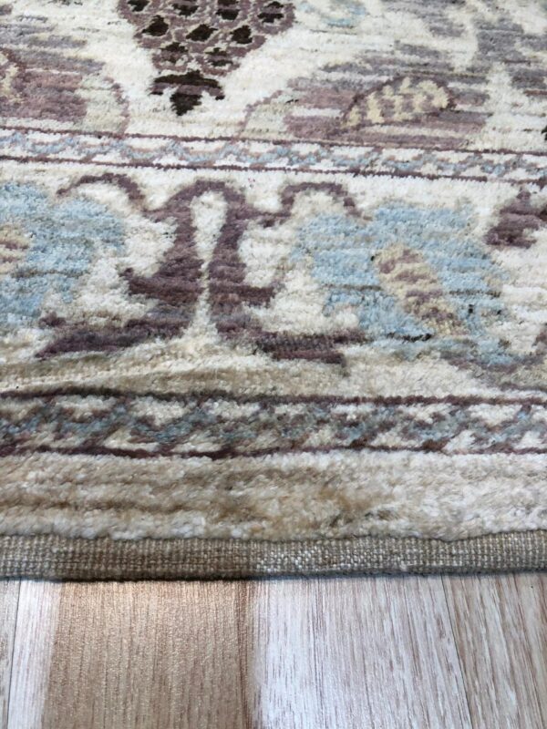 High-pile rug with cream, mauve, and blue traditional patterns rests on light plank flooring.