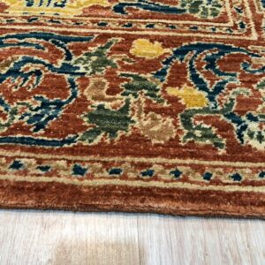 Intricate orange, teal, green, and gold patterned rug border rests on light blonde wooden flooring.