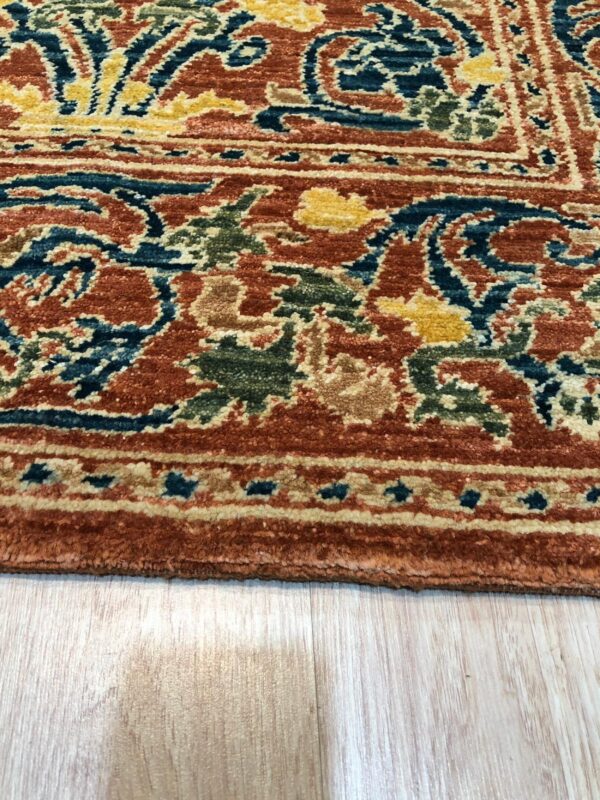 Intricate orange, teal, green, and gold patterned rug border rests on light blonde wooden flooring.