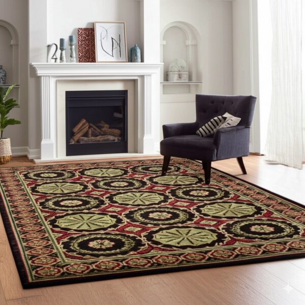 Black, red, and green ornate patterned rug on a hardwood floor by a fireplace and armchair.