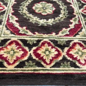 Dark brown, medium-pile rug displaying traditional red, ivory, and green floral patterns over light wood flooring.