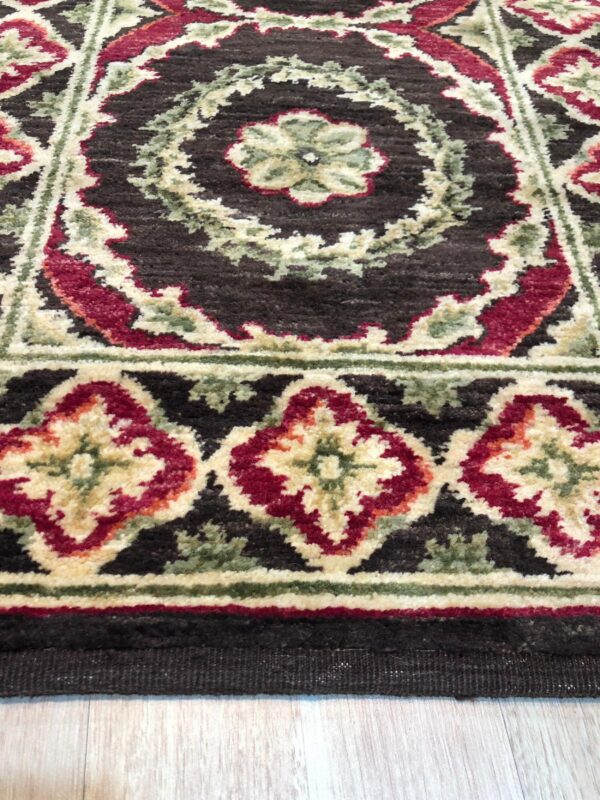 Dark brown, medium-pile rug displaying traditional red, ivory, and green floral patterns over light wood flooring.