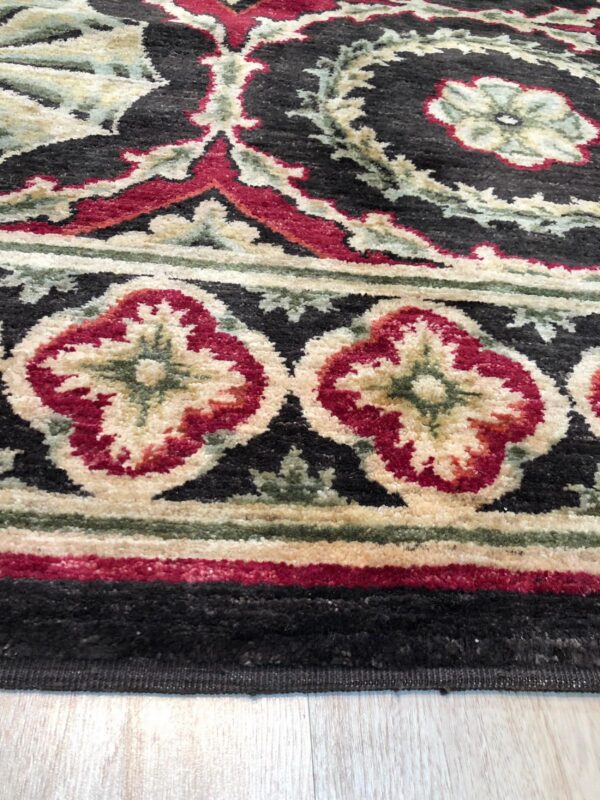 Textured rug detail in black, crimson, and cream highlights ornate floral and medallion borders on pale wood flooring.
