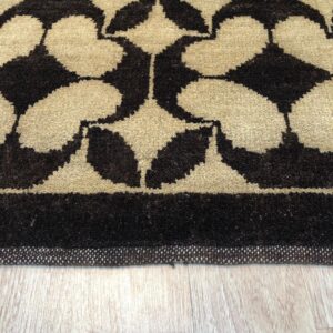 Dark brown and beige geometric medallion rug border rests on light wood grain flooring.