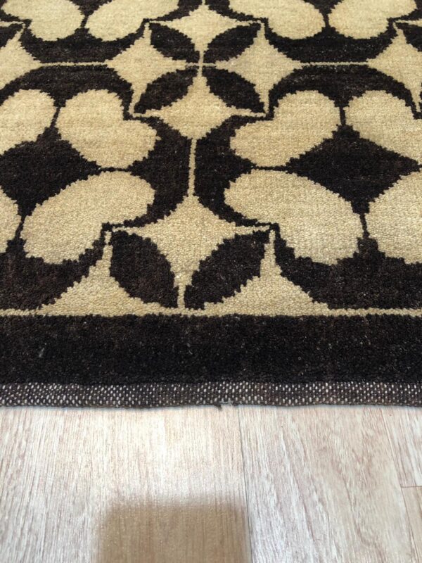 Dark brown and beige geometric medallion rug border rests on light wood grain flooring.